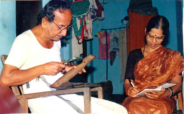Puninchathaya reading from palm manuscript and Mrs. Puninchathaya penning it down.